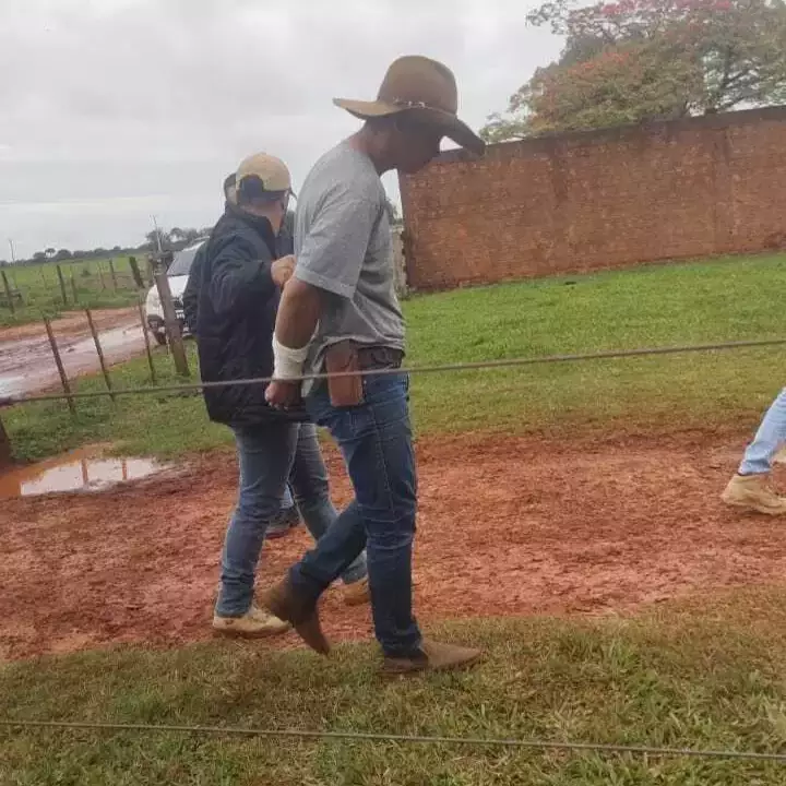 Homem de chapéu, idade média, estatura alta, sendo conduzido por policial.